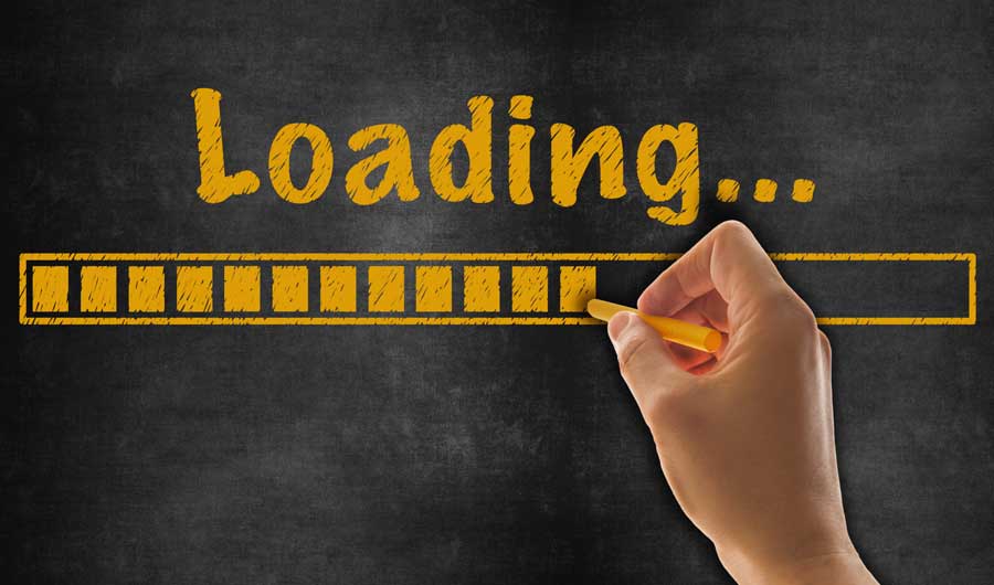 Eine Hand zeichnet mit einem gelben Stift ein Ladebalken unter dem Wort 'Loading...' auf eine schwarze Tafel, was auf die Optimierung der Ladezeiten von Websites hinweist - WordPress Ladezeiten verbessern.